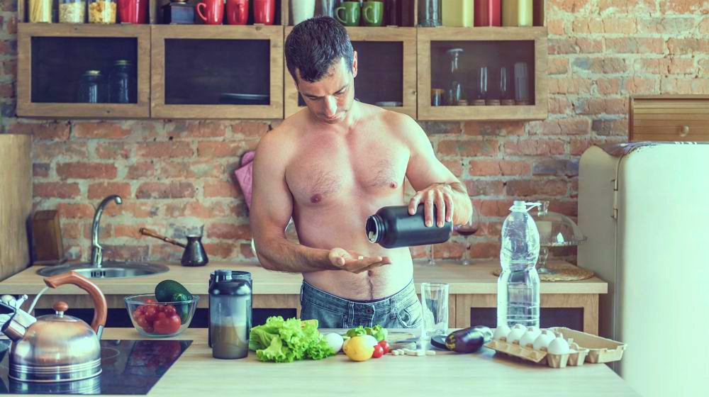 Young attractive man takes vitamin tablets for athletes in the kitchen | Featured